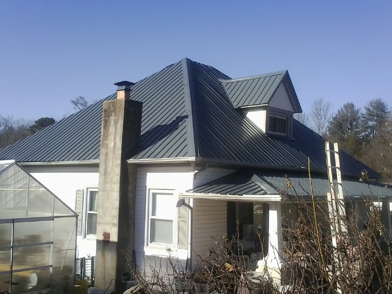 Dark blue standing seam metal roof on a white farmhouse with dormer — Slate & Tile Roof Repair by Roofing Brothers in Clifton Heights