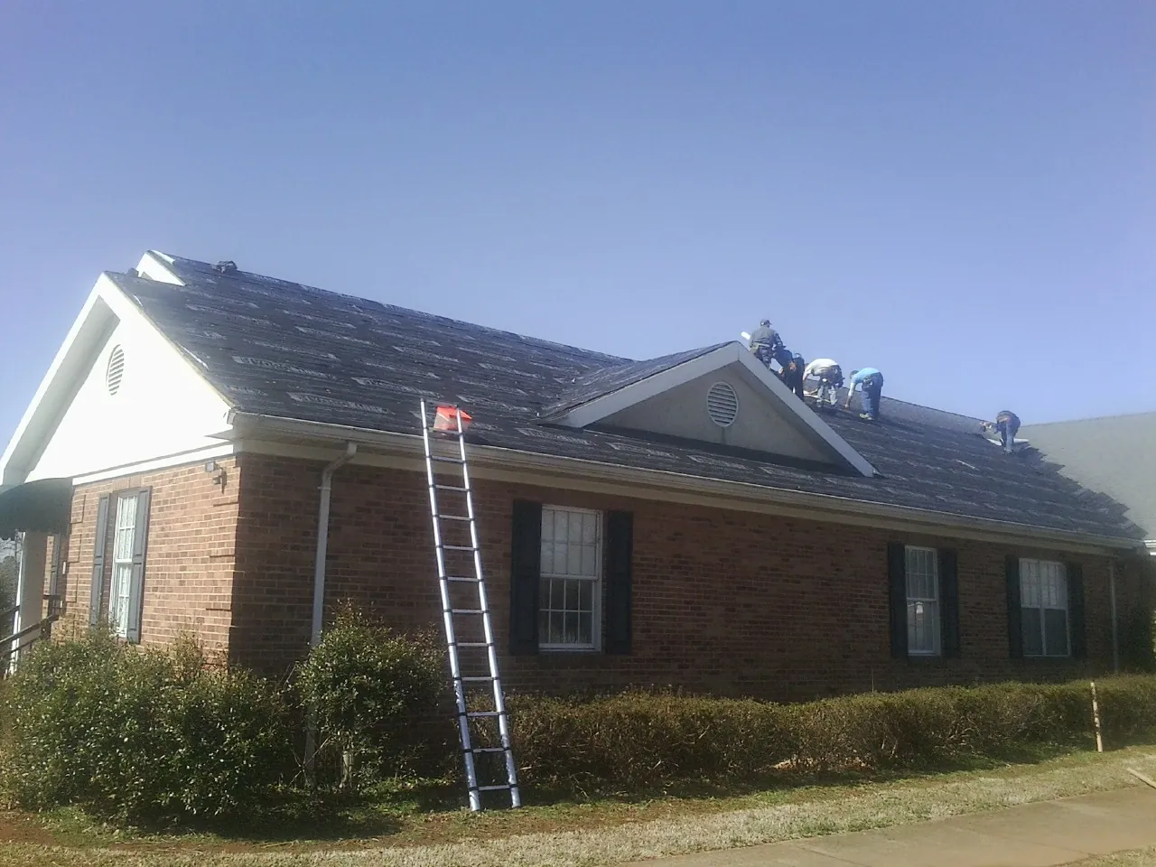 Crew tearing shingles off a brick ranch roof with a ladder set — Metal Roof Repair work by our crew in Clifton Heights