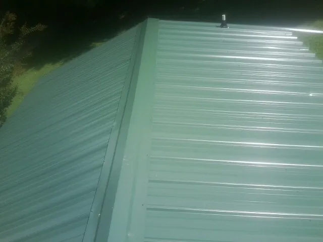 New green metal panels meeting at the ridge of a roof — Flat Roof Repair work by our crew in Clifton Heights