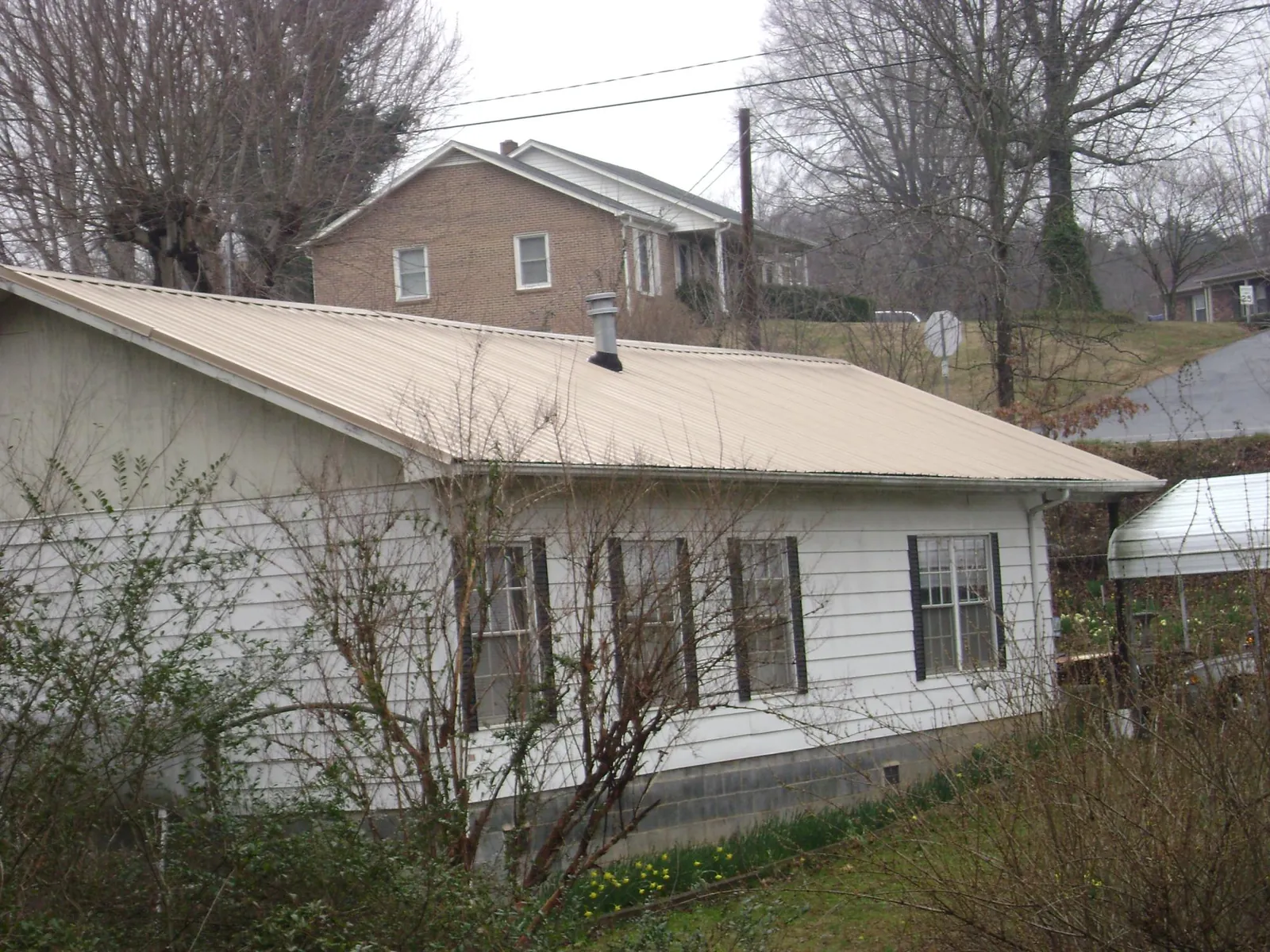 Tan metal roof on a white sided house set into a hillside — Commercial Roofing by Roofing Brothers in Clifton Heights