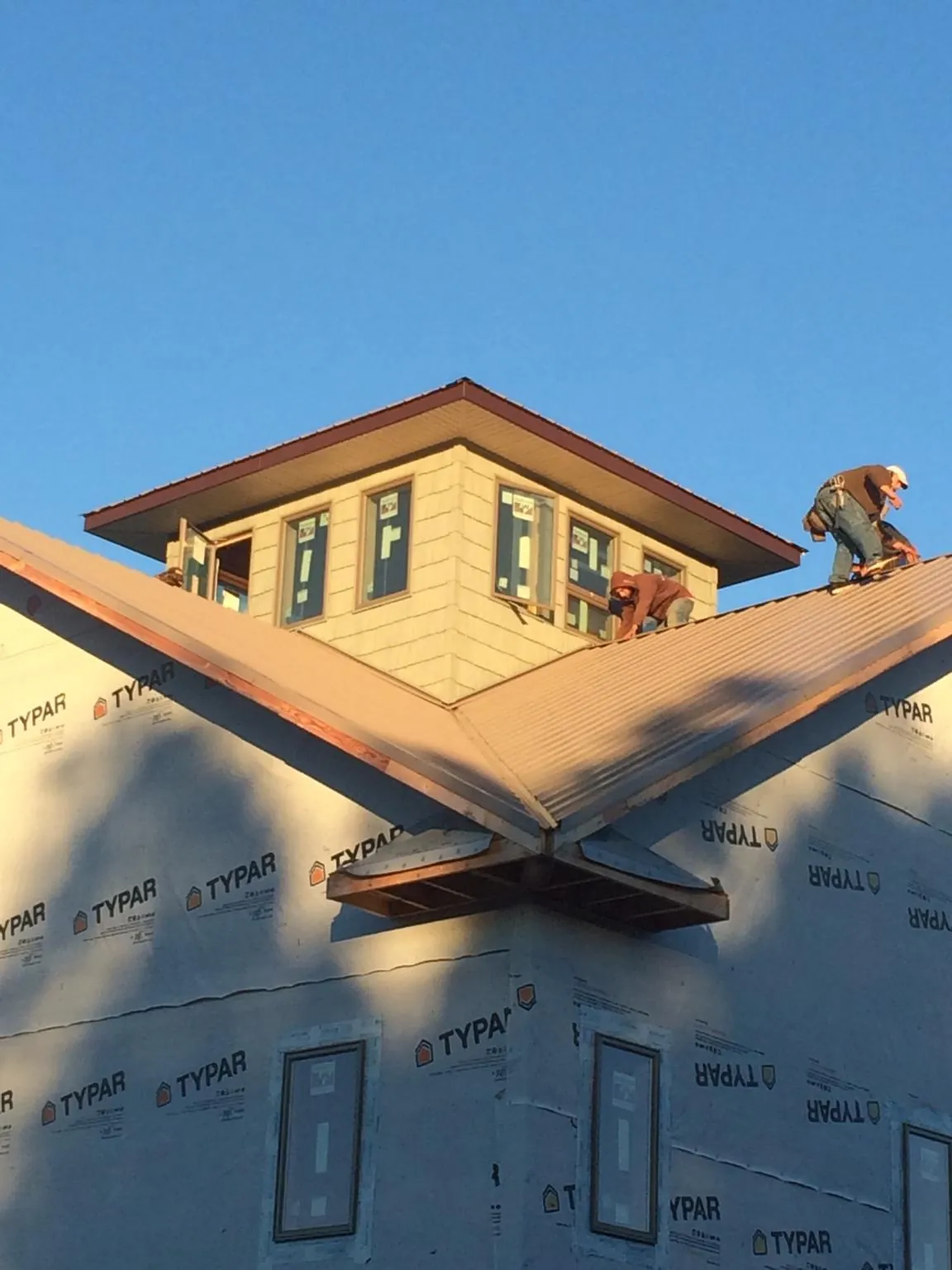 Roofers working around a rooftop cupola on a new metal roof at sunset — Roof Waterproofing in Clifton Heights by Roofing Brothers